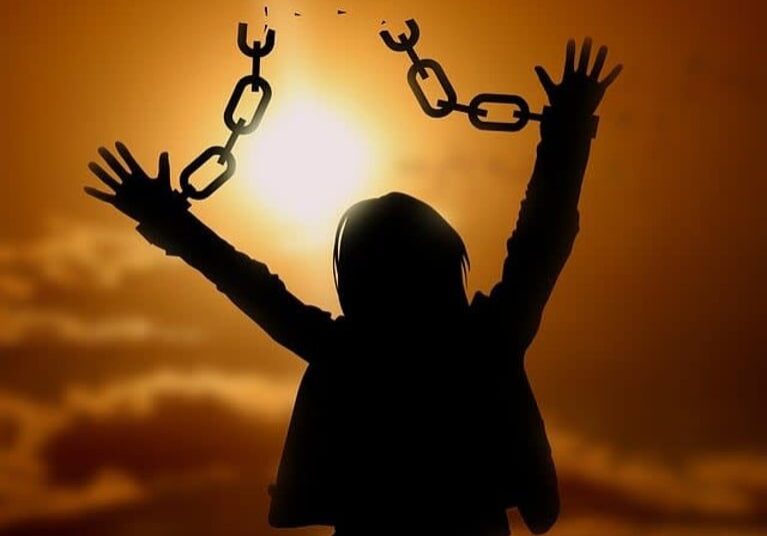Person breaking free from chains against a sunset.