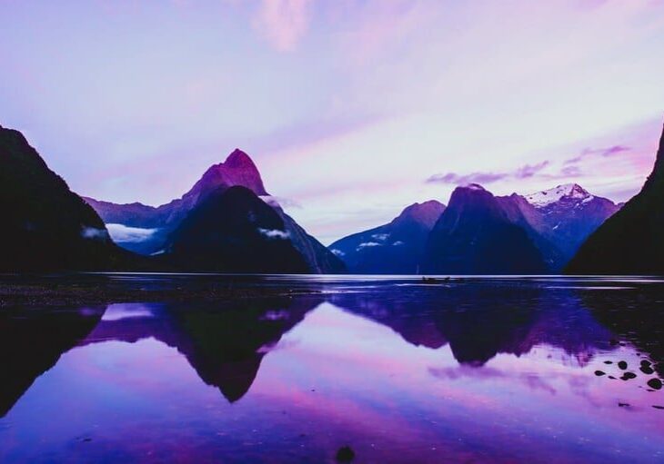 Mountain peaks reflected in calm purple-hued water at sunset.